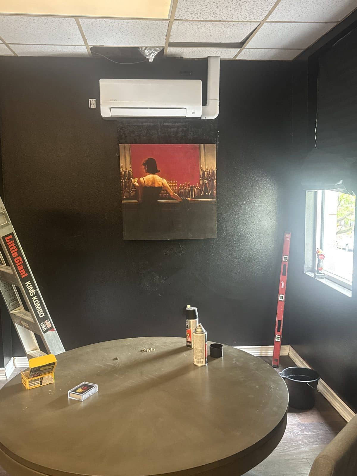 Mini-split indoor unit above a framed painting with line-set cover routed to the ceiling, ladder still in the room