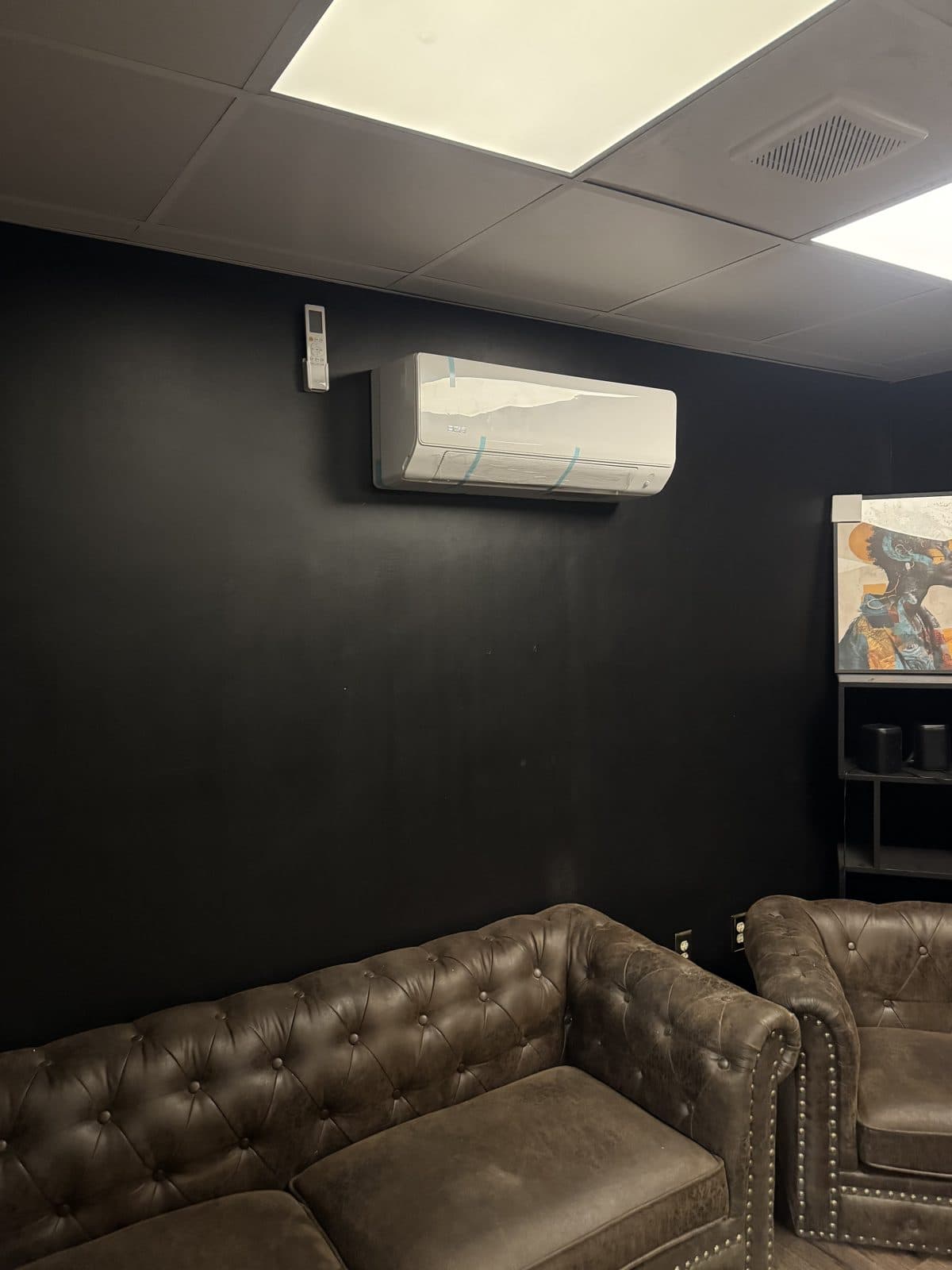 Mini-split indoor unit on a black wall above tufted leather lounge seating